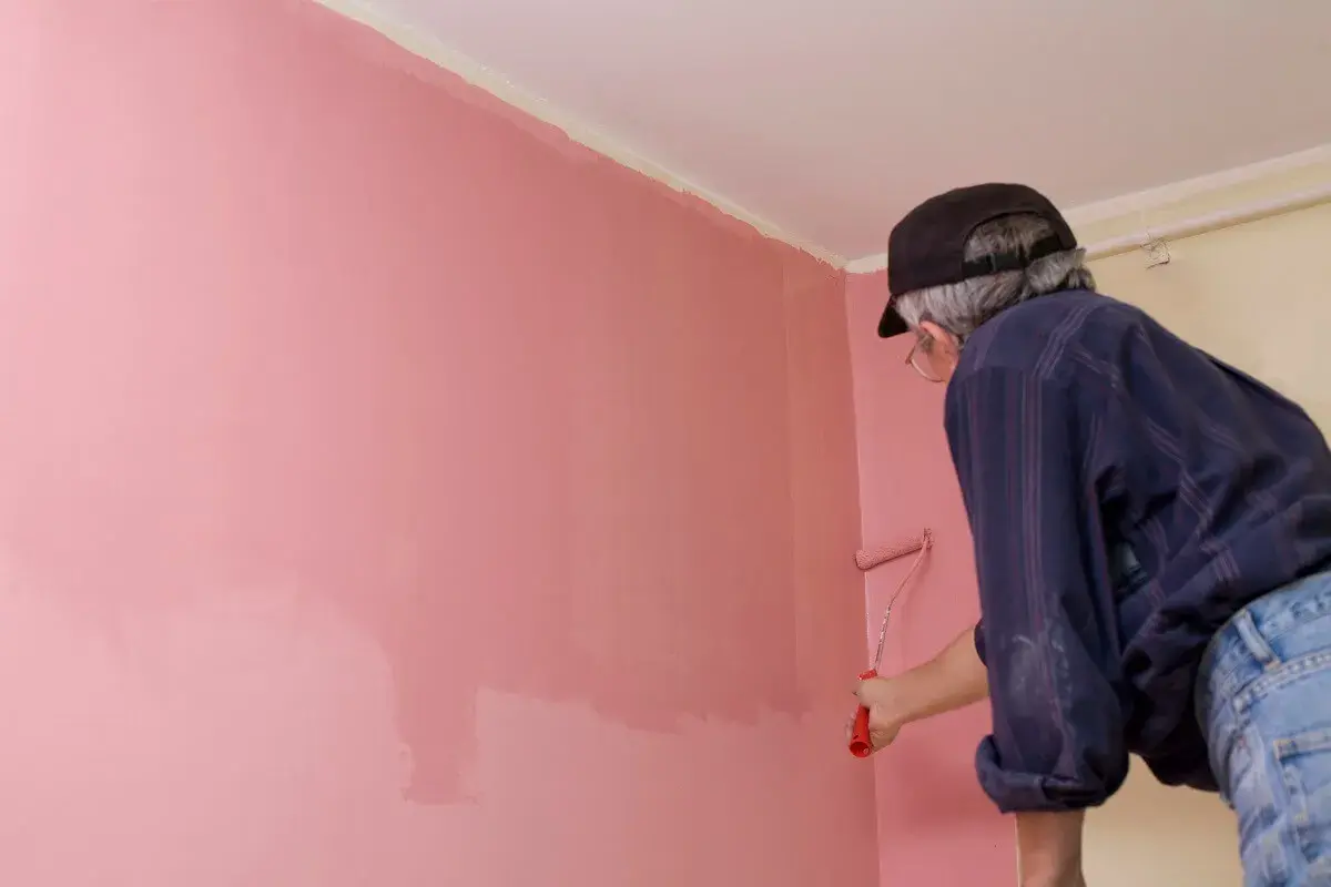 Un homme peint un mur en rose. La peinture fonce ou s'éclaircit en séchant, créant un effet subtil.