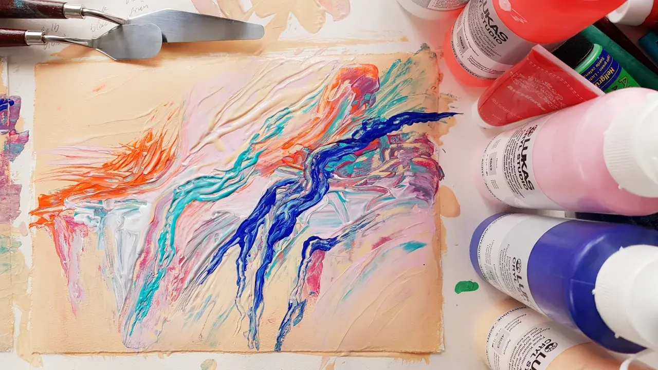 Peinture abstraite aux couleurs vives sur un support, avec des spatules et des tubes de peinture acrylique.
