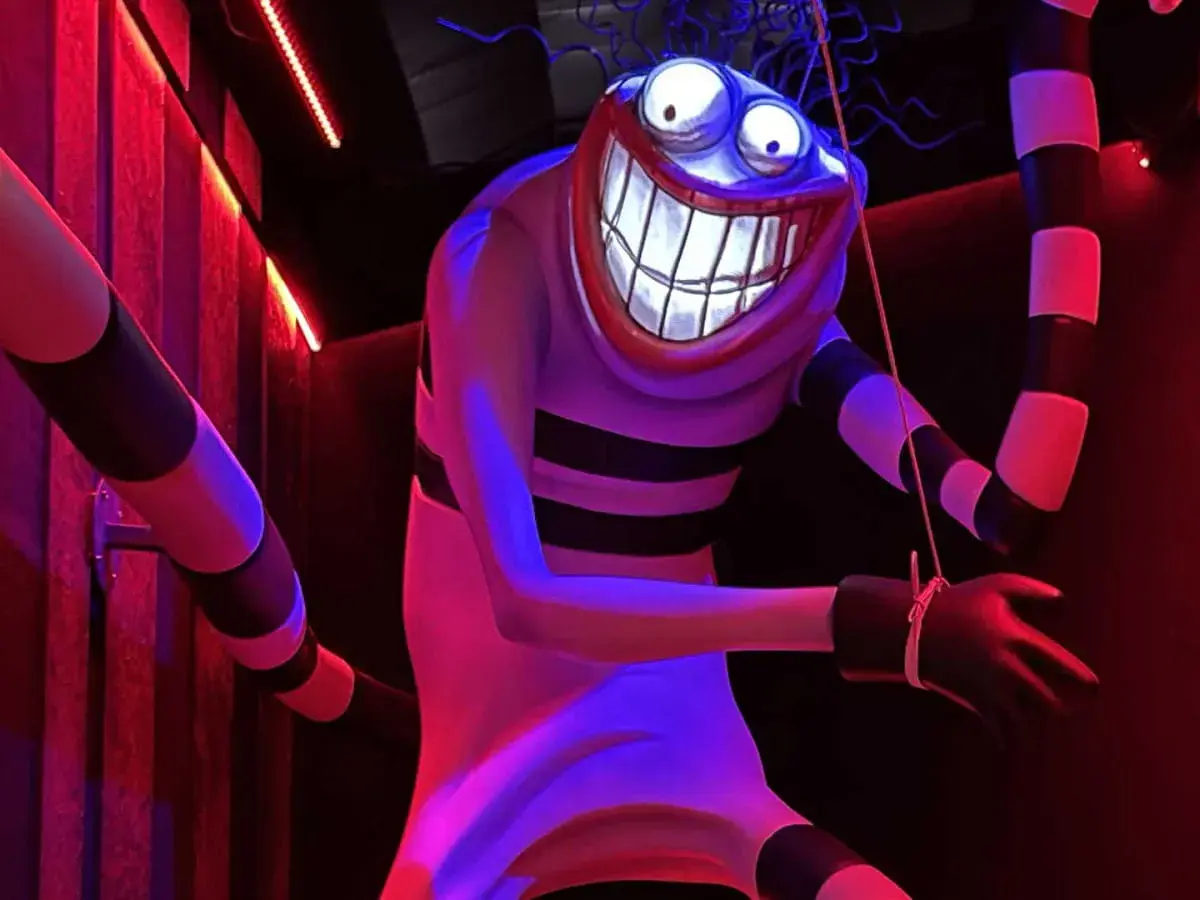 Personnage étrange au sourire démesuré, rappelant un dessin Tim Burton facile. Rayures noires et blanches, lumières rouges et bleues.
