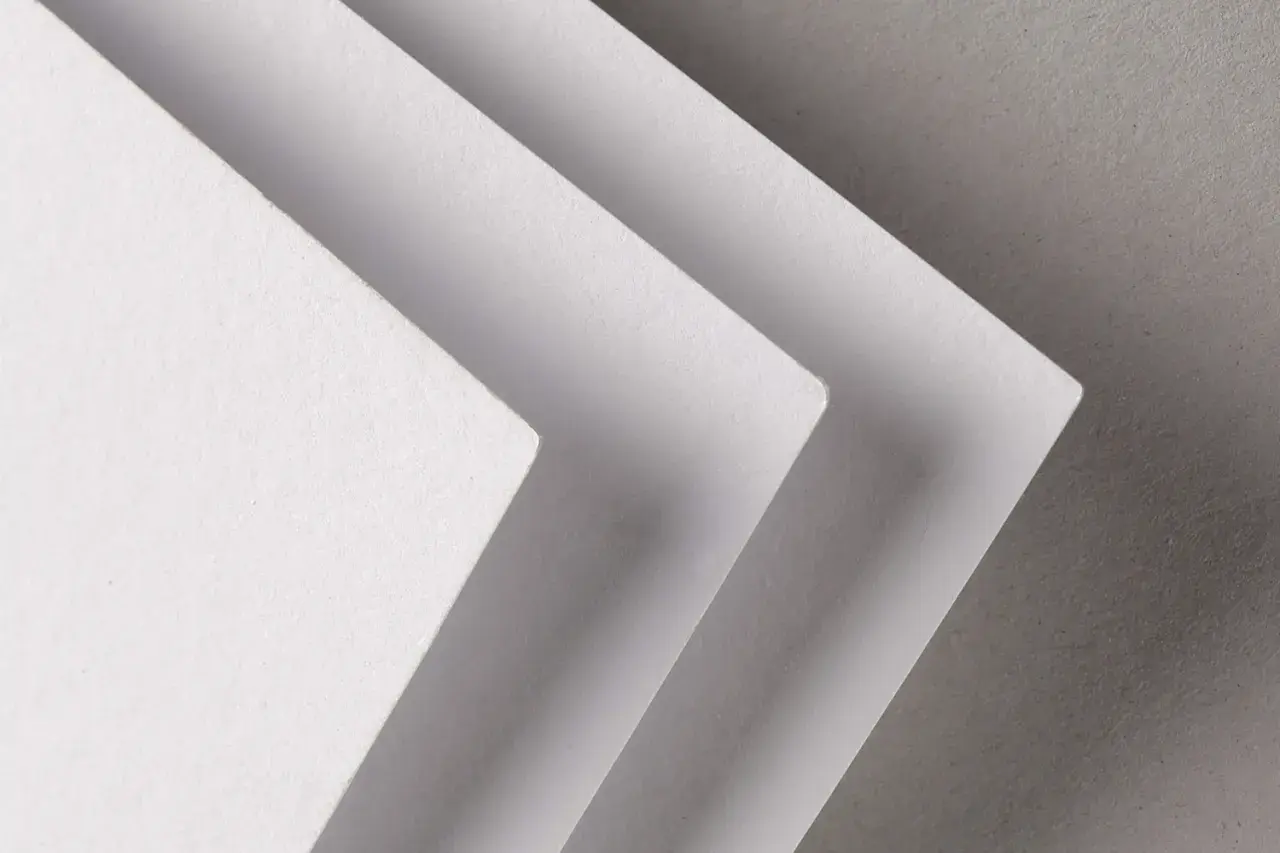 Trois feuilles de papier blanc superposées, créant un effet d'escalier. La texture du papier rappelle celle d'un **format raisin** pour une œuvre d'art.