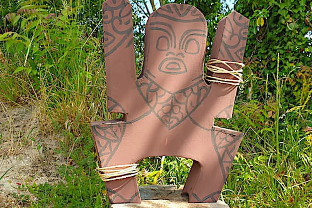 Modèle de totem à fabriquer, orné de motifs tribaux et de cordes. Il est posé dans un décor naturel verdoyant.