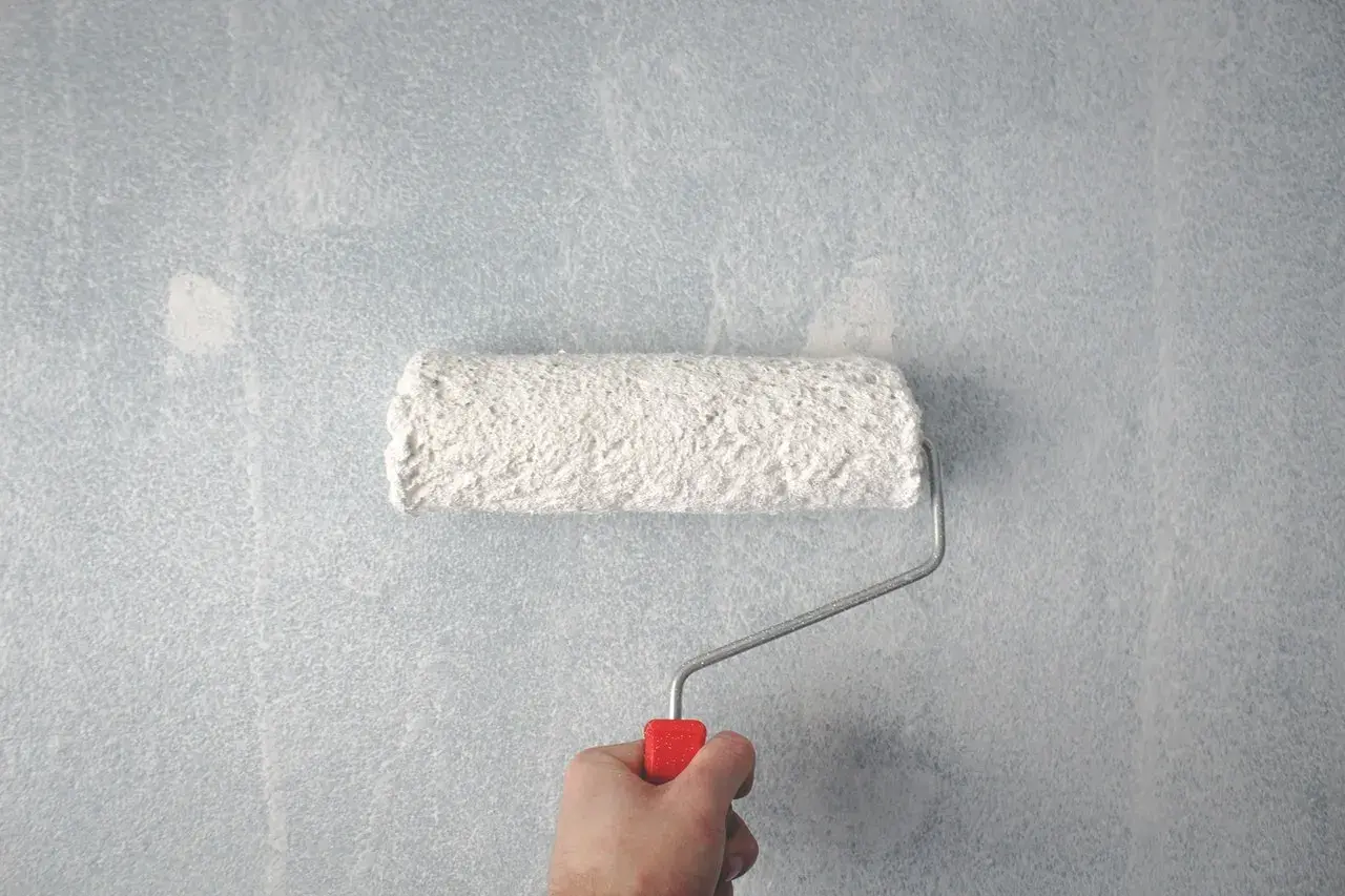 Main tenant, voici comment faire la peinture : un rouleau blanc couvre un mur bleu clair.