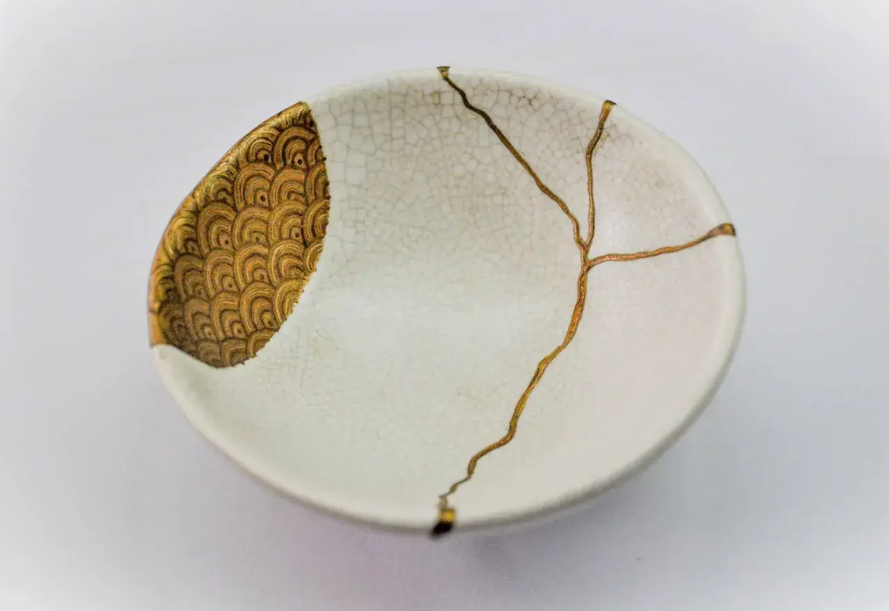 Bol blanc orné de motifs dorés, réparé avec l'art japonais de la vaisselle cassée, soulignant la beauté des imperfections.