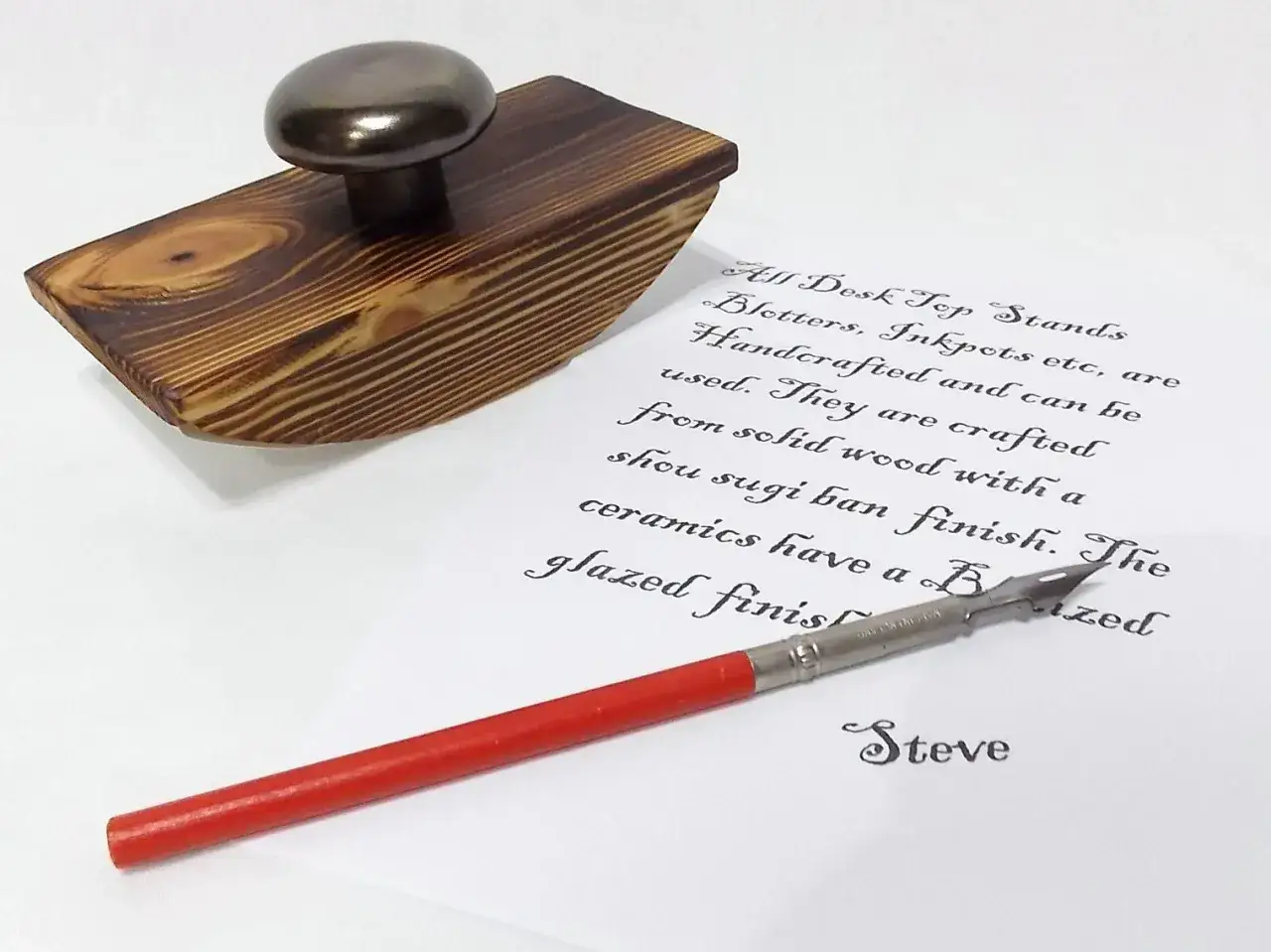Un buvard en bois avec une poign&eacute;e m&eacute;tallique, pr&ecirc;t pour son utilisation. Une plume d'&eacute;criture et un texte calligraphi&eacute; sont &agrave; proximit&eacute;.