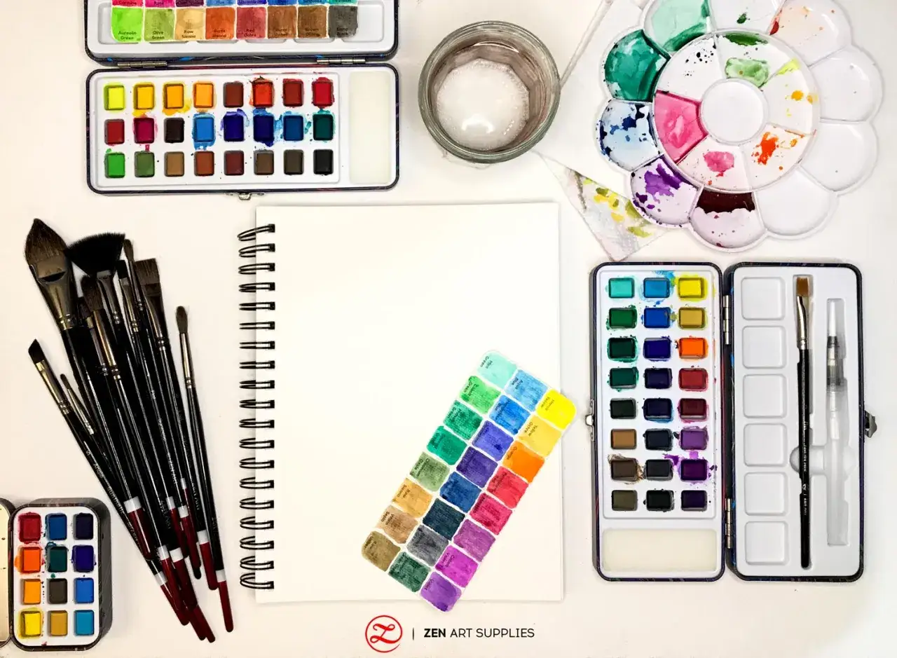 Mat&eacute;riel peinture aquarelle : palettes, pinceaux, carnet blanc et godets de couleurs vari&eacute;s pour cr&eacute;er des &oelig;uvres vibrantes.