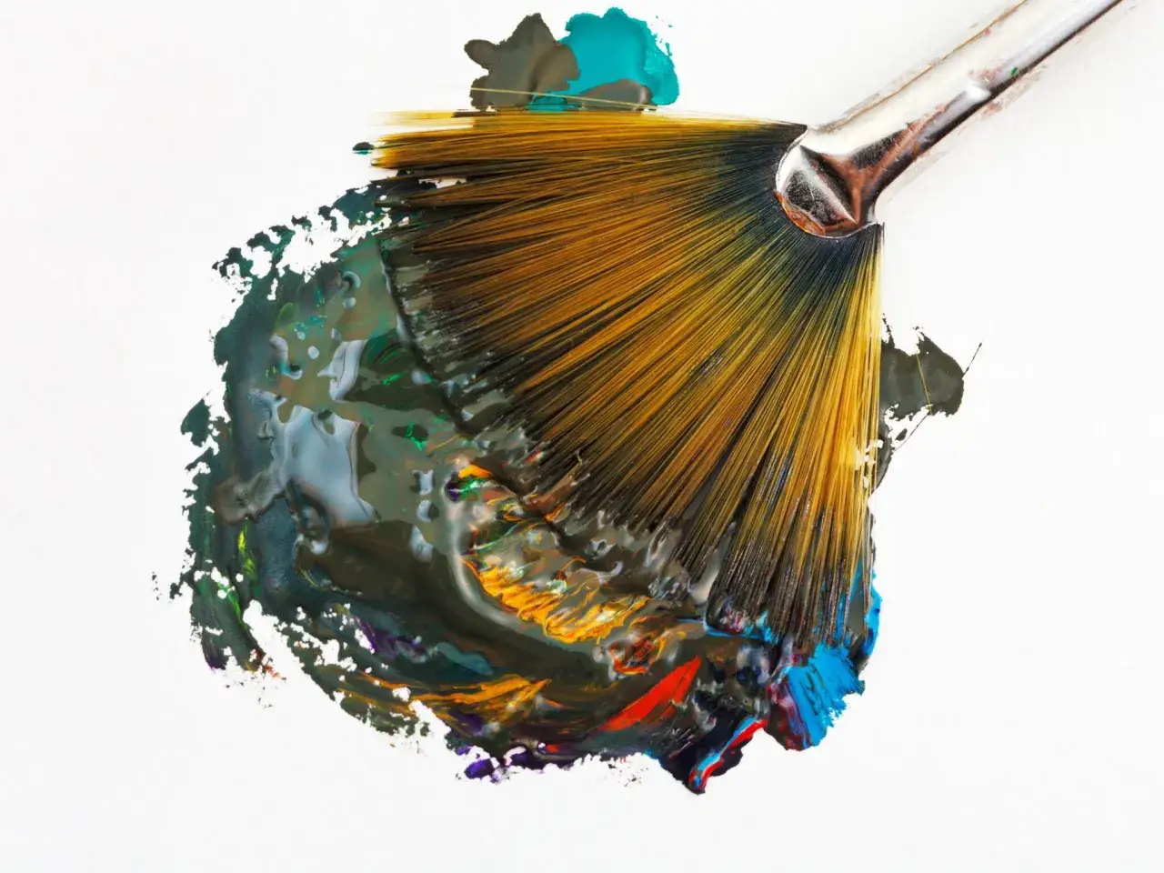 Un pinceau &eacute;ventail, charg&eacute; de peinture multicolore, cr&eacute;e des tra&icirc;n&eacute;es abstraites sur fond blanc. Son utilisation r&eacute;v&egrave;le des textures riches.