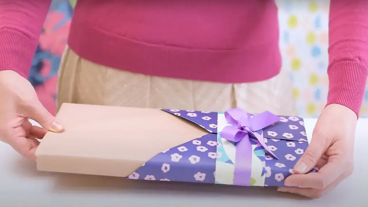 Un emballage cadeau livre, joliment d&eacute;cor&eacute; de motifs floraux violets et d'un ruban assorti, est pr&eacute;sent&eacute;.