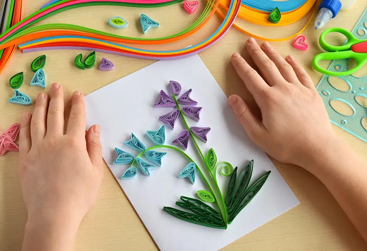 Création d'une carte fleurie en quilling pour la fête des grands-mères. Des mains d'enfant assemblent des brins de papier coloré pour former une jolie fleur.