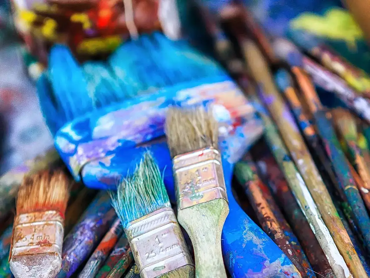Un gros plan sur des pinceaux de peinture acrylique, certains encore couverts de couleurs vives, pr&ecirc;ts pour un nettoyage.