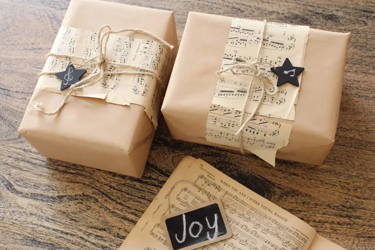 Pr&eacute;parer No&euml;l : paquets cadeaux emball&eacute;s dans du papier kraft, d&eacute;cor&eacute;s de partitions anciennes et d'&eacute;toiles noires. Cartes de v&oelig;ux 
