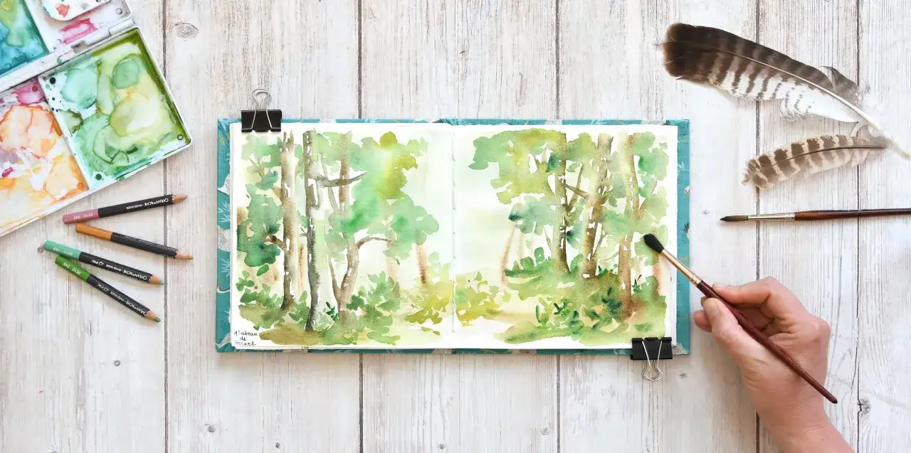 Un dessin carnet de voyage facile d'une forêt en aquarelle, avec des crayons et des plumes d'oiseaux.