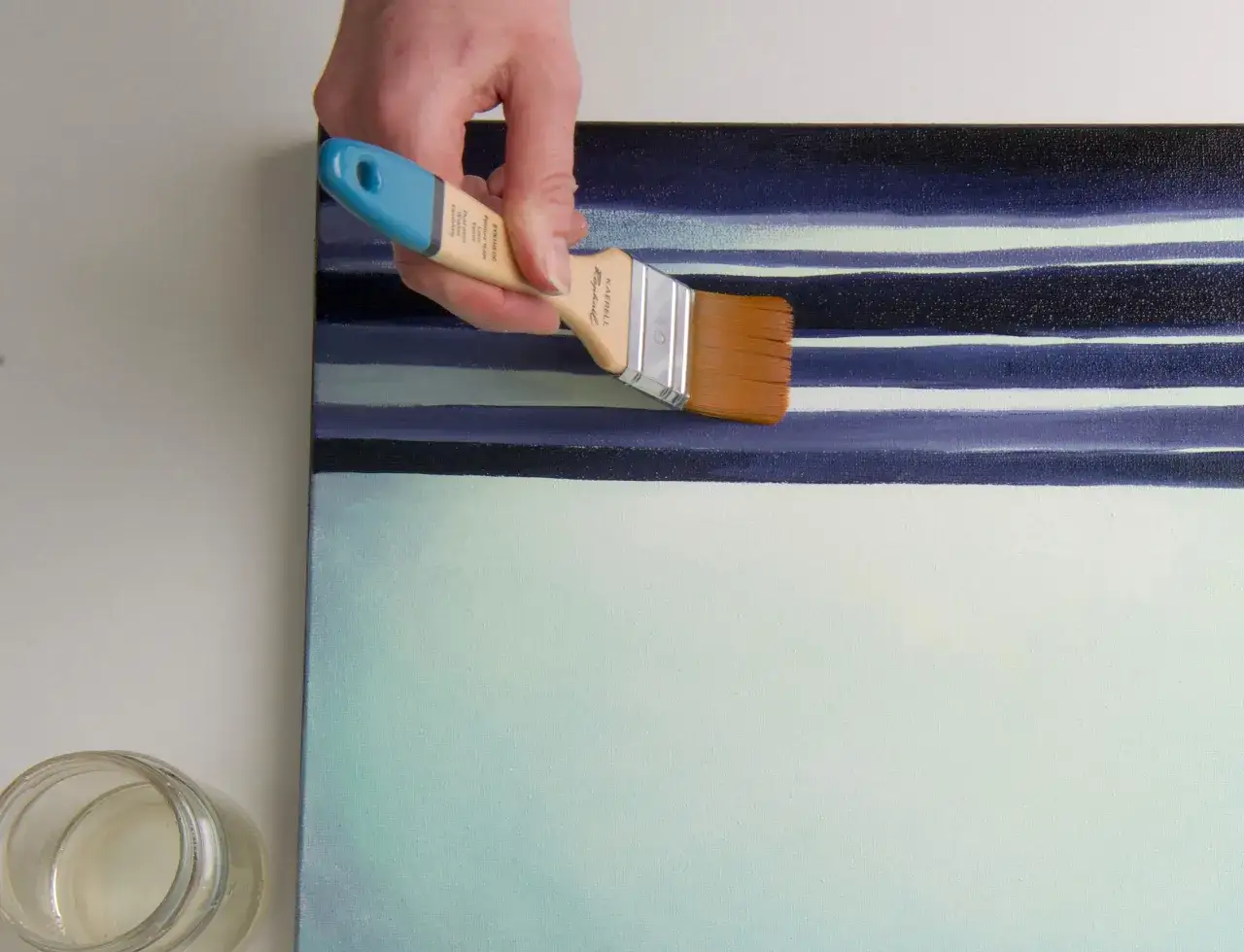 Main d'artiste appliquant du vernis &agrave; retoucher sur une toile aux rayures bleues et vertes.