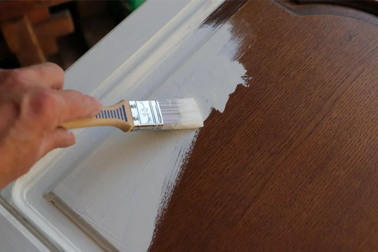 Application d'un vernis sur une peinture bois. La main tient un pinceau pour recouvrir le bois d'une couche protectrice.