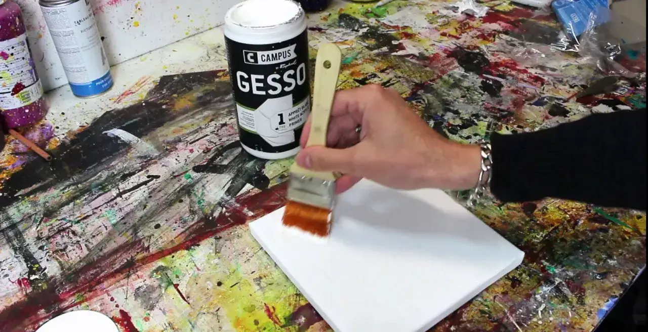 Appliquer du gesso sur une toile pour la préparer à une nouvelle création. Une main tient un pinceau imbibé de blanc pour recouvrir la surface.