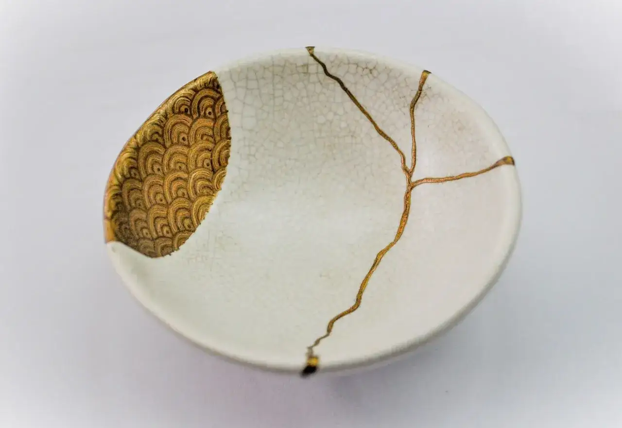 Un bol blanc craquel&eacute;, orn&eacute; d'un motif dor&eacute; en &eacute;ventail et de lignes dor&eacute;es qui suivent les fissures, illustrant l'art japonais de la vaisselle cass&eacute;e.