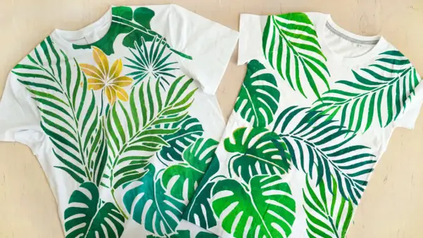 Deux tee-shirts blancs ornés d'une peinture de feuilles tropicales vertes et d'une fleur dorée.