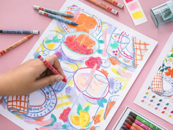 Une main colorie une scène de repas avec des pastels. Une idée art créatif pour un moment joyeux et coloré.