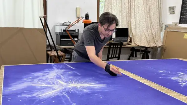 Un artiste stylo bic travaille sur une grande toile bleue, créant un motif d'étoiles filantes.