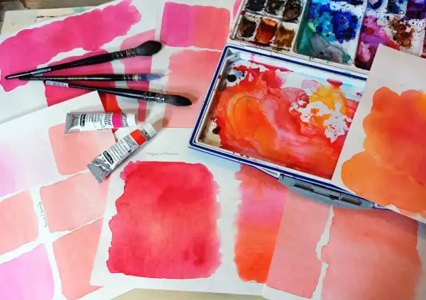 Des carrés de feutre aquarelle aux teintes roses et orangées, des tubes de peinture et des pinceaux. L'utilisation du feutre aquarelle est mise en avant.