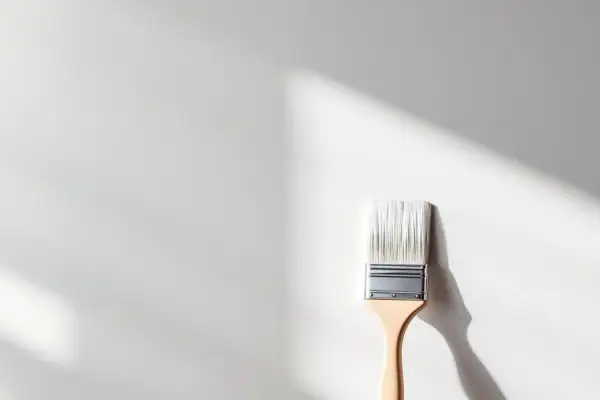 Pinceau neuf prêt à appliquer une peinture pour plastique sur une surface blanche, avec des ombres douces projetées par la lumière.