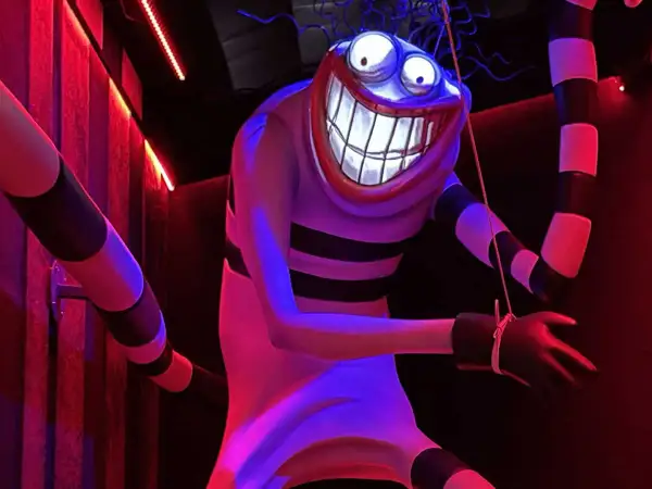 Personnage étrange au sourire démesuré, rappelant un dessin Tim Burton facile. Rayures noires et blanches, lumières rouges et bleues.