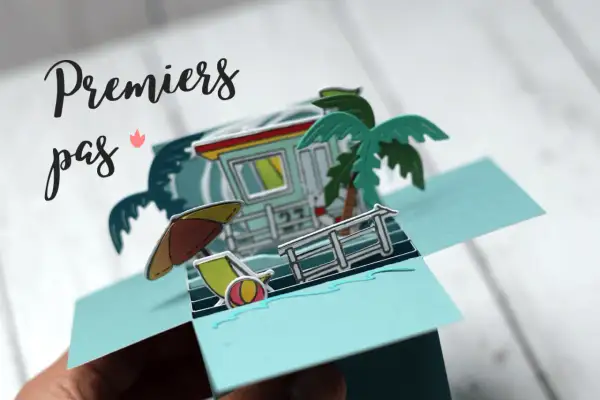 Carte pop-up plage avec cabine de sauveteur, palmier, parasol et transat.
