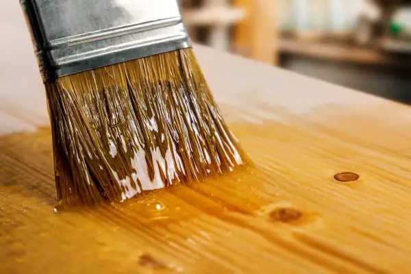 Un pinceau applique du vernis sur une planche de bois. Le vernis brillant reflète la lumière. Quel pinceau pour vernis bois ?