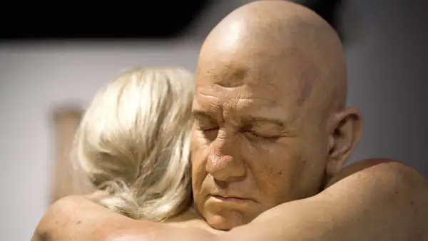 Un homme chauve aux yeux clos est étreint par une femme aux cheveux blonds. Une œuvre saisissante d'un peintre hyperréaliste français.