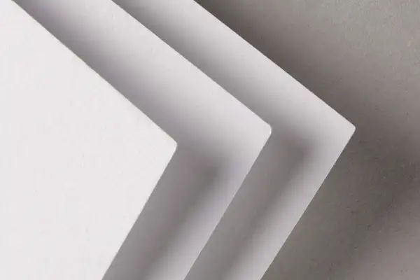 Trois feuilles de papier blanc superposées, créant un effet d'escalier. La texture du papier rappelle celle d'un **format raisin** pour une œuvre d'art.