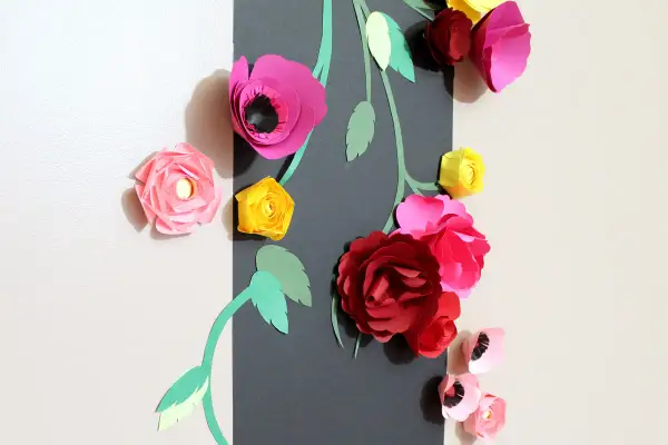 Un bouquet de fleurs en papier Canson aux couleurs vives, roses, rouges et jaunes, orne un mur.