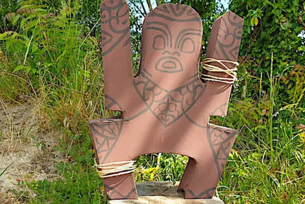 Modèle de totem à fabriquer, orné de motifs tribaux et de cordes. Il est posé dans un décor naturel verdoyant.