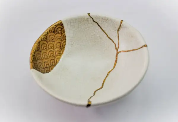 Bol blanc orné de motifs dorés, réparé avec l'art japonais de la vaisselle cassée, soulignant la beauté des imperfections.