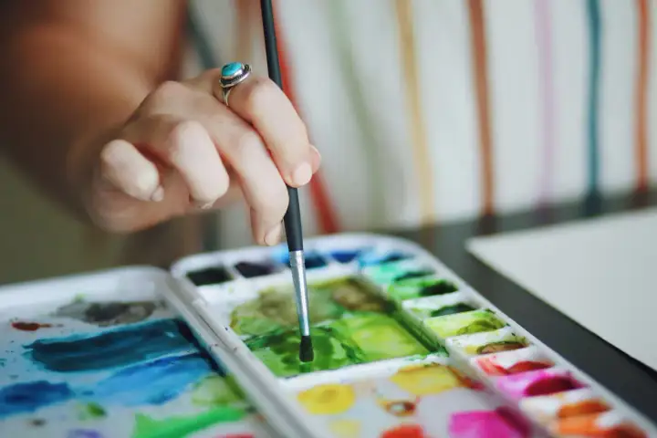 Main d'une artiste utilisant la technique pastel sec pour mélanger des couleurs vives sur une palette.